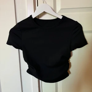 Svart croppad ribbad topp - En svart croppad topp med korta ärmar och rund hals. Toppen är ribbad vilket ger en snygg struktur och sitter tajt mot kroppen. Perfekt att matcha med höga jeans eller kjol för en clean look.