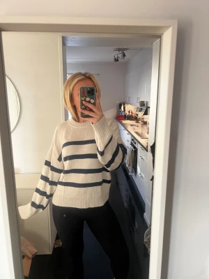 Vit och marinblå randig stickad tröja - Säljer en mysig stickad tröja i vit med breda marinblå ränder. Tröjan har rund hals, långa ärmar och ribbade muddar vid ärmslut och nederkant. Perfekt för dig som gillar en chill och stilren look med lite oversized känsla.