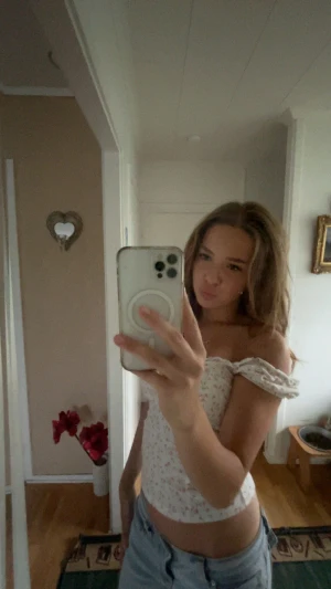 Vit blommig korsett-topp - Vit korsett-topp med små rosa blommor och omlott-detalj. Toppen har offshoulder-ärmar med volang och en figurnära passform som framhäver midjan. Säljs för ca 200, kan inte exakta orginalpriset men det ligger runtomkring 200 kronor. 🤗