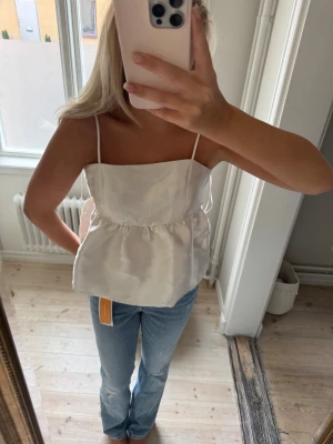 Vit söt topp med tunna axelband - Supersöt vit topp med tunna axelband och lätt rynkad midja. Toppen har en luftig och lite croppad passform som ger en fräsch och somrig vibe. Perfekt att styla med jeans eller kjol för en chill look.lapp kvar 