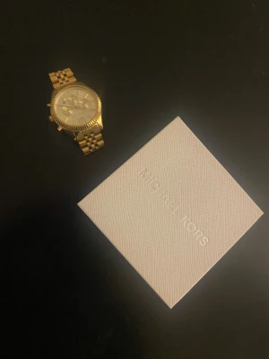 Guldfärgad klocka Michael Kors - Säljer en snygg guldfärgad klocka från Michael Kors med länkarmband i metall och rund urtavla. Klockan har romerska siffror, tre mindre visartavlor och datumvisning. Kommer med originalask. Perfekt accessoar för dig som gillar stilrena detaljer. Priset kan diskuteras vid snabb affär!