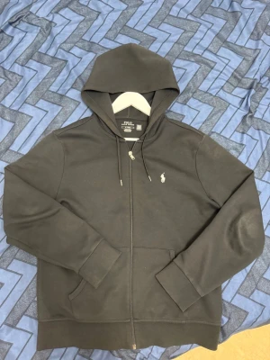 Svart hoodie från Polo Ralph Lauren - Svart hoodie från Polo Ralph Lauren i storlek M. Tröjan har huva med snörning, dragkedja framtill och två fickor. Klassisk Polo-logga broderad på bröstet. Tillverkad i mjuk bomull för skön komfort och stilren look.jag köpte den för 2,2 från Zalando kan diskutera pris 