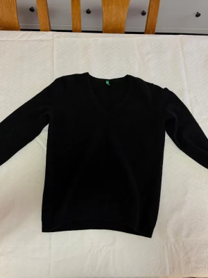 Svart v-ringad tröja från Benetton - Svart v-ringad tröja från United Colors of Benetton med broderad logga framtill. Tröjan är stickad i mjukt material och har långa ärmar med ribbade muddar. Perfekt för dig som gillar stilrena och klassiska plagg med enkel design.