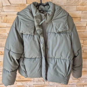 Grön pufferjacka från FB Sister - Inköpt föra året men har aldrig haft på mig den. Atorleken är M men passar även nån med storlek S. Snygg pufferjacka i kahki färg från FB Sister. Jackan har huva, dragkedja framtill och tryckknappar. Perfekt för kalla dagar när du vill vara både varm och trendig.