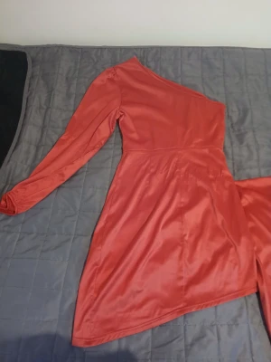 Röd oneshoulder klänning från SHEIN - Snygg röd kortklänning från SHEIN med glansig finish. Klänningen har ett unikt oneshoulder-snitt med lång ärm på ena sidan och ärmlös på andra. Tillverkad i mjuk polyester som ger en lyxig känsla och sitter bekvämt. Perfekt för dig som vill sticka ut med en cool asymmetrisk look.