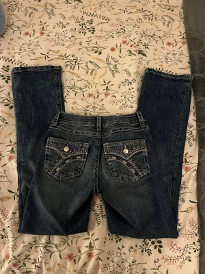 Blå jeans från Gina Tricot - Snygga mörkblå jeans från Gina Tricot med coola broderade detaljer och silvriga knappar på bakfickorna. Klassisk femficksmodell med kontrastsömmar och rak passform. Säljer då de inte sitte their rätt tyvärr💓