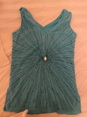 Glittrig blå topp  - Snygg topp med glittriga detaljer o en kristall i mitten. Köpt second hand vet ej vilket märke de är. Skulle säga att det passar en S/XS  
