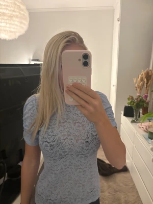 Ljusblå spetsblus med puffärm - Säljer en ljusblå blus i spets med korta puffärmar. Blusen har ett detaljerat blommigt spetsmönster 