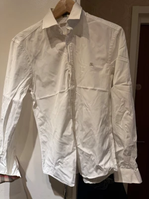Burberry Skjorta - Säljer denna vita Burberry skjorta som jag använt vid ett fåtal tillfällen. Skjortan har den ikoniska Burberry materialet vid ärmarna samt kragen som passar fint till kommande nyårs firande. Storleken passar bägge S samt M