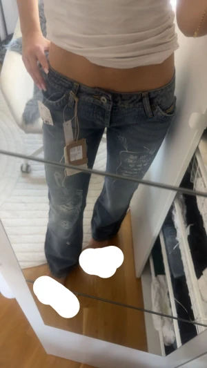 Lågmidjade blå jeans med tryck - Säljer ett par blå jeans med låg midja och coola vita tryckdetaljer på benen. Jeansen har en avslappnad passform och slitna partier för en trendig look. Perfekta för dig som gillar streetstyle och vill sticka ut lite extra. XS men passar S