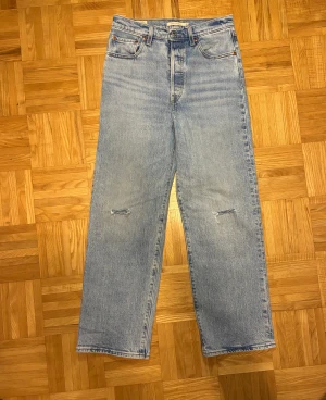 Levi's 551 ljusblå jeans W28 L27 - Ljusblå Levi's 551 jeans med hög midja och raka ben. Jeansen har klassiska fem fickor, slitna detaljer vid knäna och en chill, loose passform. Tillverkade i jeansmaterial med vintage vibe och snyggt Levi's-märke bak på linningen.
