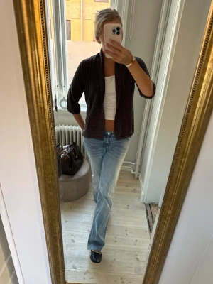 Mörkgrå ribbad kofta med sjalkrage - Säljer en mörkgrå ribbad kofta med sjalkrage och trekvartsärm. Koftan är stickad och har en loose passform som gör den skön att bära över en topp eller t-shirt. Perfekt för lager-på-lager under höst och vår. Enkel och stilren design.