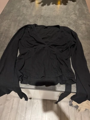 Svart omlottopp från Gina Tricot - Säljer en svart omlottopp från Gina Tricot i storlek XS. Toppen har långa ärmar, v-ringad hals och knyt i midjan för en snygg siluett. Materialet är mjukt och lätt, perfekt för att styla med jeans eller kjol. En klassisk och stilren topp som funkar året runt.💞💞