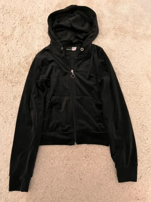 Svart velour hoodie med dragkedja - Svart hoodie från Gina tricot i mjuk velour med dragkedja och huva. Jackan har långa ärmar, ribbade muddar och en stor ficka framtill. Perfekt för chill dagar och streetstyle. Snygg croppad passform som ger en modern vibe.