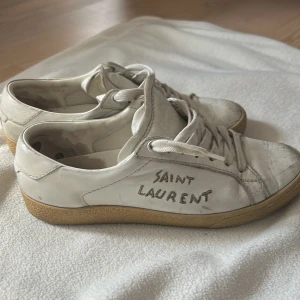  Saint Laurent - Vita sneakers från Saint Laurent med klassisk låg profil och snörning. Skorna har en beige sula och handskriven logga på sidan. Tillverkade i skinn. platt sula. Perfekta för en stilren och avslappnad look.
