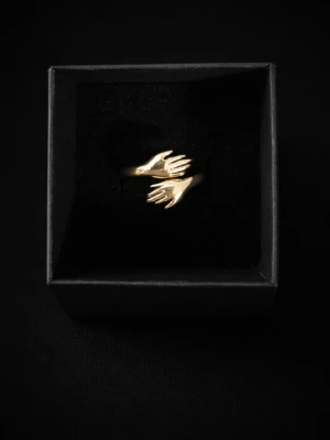 Guldfärgad ring med handmotiv - Unik guldfärgad ring i metall med två händer som motiv. Ringen har en öppen design och levereras i en svart ask. Perfekt för dig som gillar annorlunda och kreativa smycken.