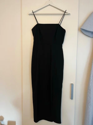 Svart långklänning med smala axelband - En svart långklänning från Zara i storlek S. Den är figurformad med smala axelband och en slits på vänstra benet. Slitsen har lite slitage men annars är klänningen som ny.