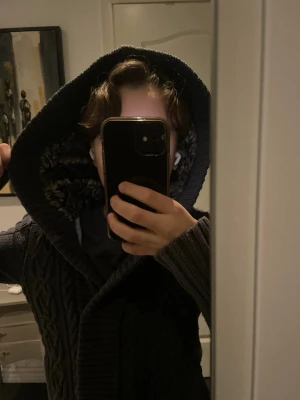 Mörkblå stickad kofta med huva - Mysig mörkblå stickad kofta med huva och fuskpäls runt kanten. Koftan har långa ärmar, knappar framtill och ett snyggt kabelstickat mönster. Perfekt för kyliga dagar när du vill vara både varm och stilren. Skulle säga att den passar Xxs/Xs. Kolla måttet. Har ett ganska stort hål men det påverkar absolut ingenting. Syns inte och det är lika varmt.