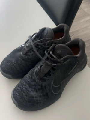 Svarta Nike sneakers med mesh - Snygga helsvarta Nike sneakers med mesh-överdel och diskret swoosh på sidan. Skorna har snörning och en lätt, flexibel sula som passar perfekt för en aktiv livsstil. Stilren design med sportig känsla och bekväm passform. Crossfit skor!!Använda men inte använt på ett bra tag, därför säljer jag dom. Köp gärna!