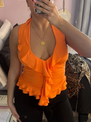 Orange omlottopp med volang och knyt - Säljer en orange omlottopp med djup v-ringning, volangkant och knyt i nacken. Aldrig använd.