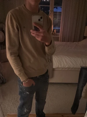 Beige tröja från Gant - Snygg beige tröja från Gant med rund halsringning och diskret logga broderad på bröstet. Tröjan har långa ärmar och ribbade muddar vid ärmslut och nederkant. Perfekt att matcha med jeans för en clean look.