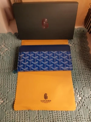 Blå Goyard plånbok med mönster - Snygg blå plånbok från Goyard med ikoniskt vitt och blått grafiskt mönster. Plånboken har dragkedja runtom och är tillverkad i ett tåligt material med exklusiv känsla. Perfekt för dig som vill ha något unikt och stilrent i väskan.