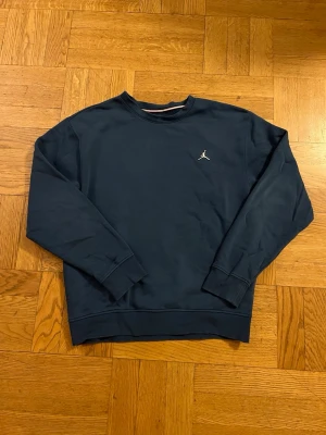Mörkblå crewneck från Jordan - Mörkblå sweatshirt från Jordan med klassisk crewneck och liten vit Jumpman-logga på bröstet. Tröjan har långa ärmar, ribbade muddar och är gjord i mjukt bomullsmaterial. Perfekt för en avslappnad och sportig stil.