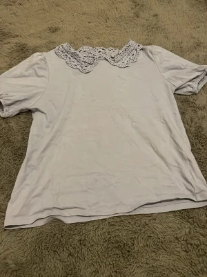 Blå topp med spetskrage - Söt vit topp med korta ärmar och en detaljerad virkad spetskrage som ger en romantisk touch. Perfekt att styla med jeans eller kjol för en trendig look. Materialet känns mjukt och bekvämt mot huden.