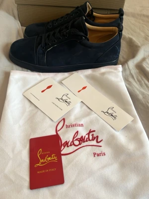 Mörkblå sneakers från Christian Louboutin - Snygga mörkblå sneakers från Christian Louboutin i mocka med klassisk låg siluett och rund tå. Skorna har svarta snören och diskreta sömdetaljer. Insidan är beige och sulan är svart. Perfekta för dig som vill ha en exklusiv och stilren look.