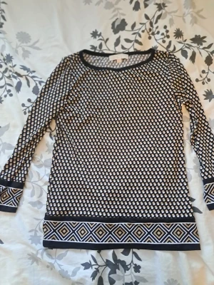 Mönstrad långärmad topp från Cream - Säljer en mycket fin långärmad tröja/topp från MICHAEL Michael Kors. Toppen har ett klassiskt svartvitt geometriskt mönster (små prickar/rutor) och en dekorativ bård med ett snyggt grekiskt inspirerat mönster i nederkant samt vid ärmsluten. Perfekt för både kontoret och mer uppklädda tillfällen! Märke: MICHAEL Michael Kors Storlek: XS (Passar även en mindre Small då materialet är stretchigt) Färg: Svart, vit och guld/beige detaljer Skick: Mycket gott skick, väl omhändertagen.
