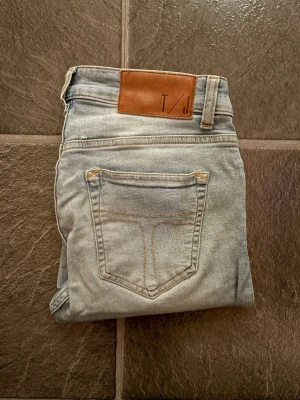 Ljusblå skinny jeans från Tiger of sweden - Snygga ljusblå skinny jeans från T/J med klassisk femficksdesign och läderpatch i midjan. Jeansen har smal passform och är perfekta för en avslappnad men trendig look. Tillverkade i mjukt denimtyg för extra komfort.