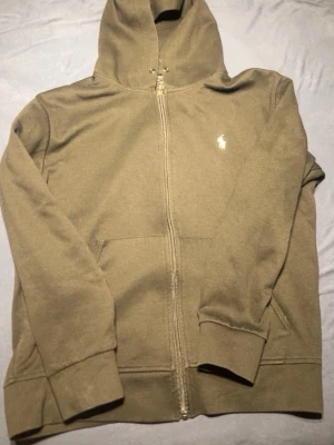 Svart kofta från Ralph Lauren - Säljer en svart kofta från Ralph Lauren med dragkedja framtill och klassisk logga på bröstet. Tröjan har huva med dragsko och två fickor framtill. Perfekt för en avslappnad och stilren look.