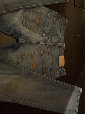 Blå jeans med kontrastsömmar - Säljer ett par klassiska blå jeans med snygga kontrastsömmar på bakfickorna. Jeansen har rak passform och normal midja, tillverkade i slitstarkt denimtyg. Perfekta för dig som gillar en tidlös och enkel stil.