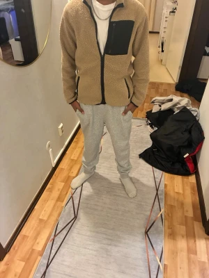 Teddyjacka - Säljer en beige teddyjacka med svart bröstficka och svarta detaljer längs dragkedjan. Den är jätte snygg och jätteskön!