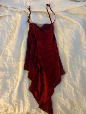 Vinrött linne H&M - Säljer ett vinrött linne från H&M med tunna axelband och asymmetrisk nederkant. Linnet har en elegant silkeslook och är perfekt för dig som vill sticka ut. Enkel men ändå stilren design som ger en lyxig känsla.
