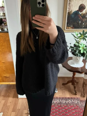 Svart stickad tröja med öppen rygg och knytning - Mysig svart stickad tröja med avslappnad passform och långa ärmar. Perfekt att slänga på sig över en t-shirt eller klänning. Enkel och stilren design utan synliga loggor eller detaljer. Fler bilder finns