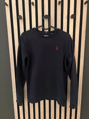 Mörkblå sweatshirt från U.S. Polo Assn. - Tjena! Säljer min mörkblå sweatshirt med rund hals från U.S. Polo Assn. Tröjan har en broderad röd logga på bröstet och ribbade muddar vid ärmslut och nederkant. Perfekt för en avslappnad och stilren look. Kontakta mig vid frågor 😁