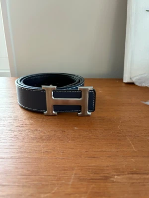 H bälte - H bälte helt nyt Blåt med vita sömar och silvrig H logga