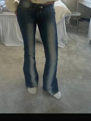 Trendiga Blåa jeans, såkallade kvarg jeans - Snygga blå bootcut jeans med ljusa slitningar längs benen. Jeansen har låg midja och klassisk femficksdesign. Perfekta för en avslappnad och trendig look..