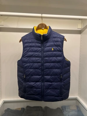 Ralph Lauren reversible väst - En riktigt fin väst ifrån Ralph Lauren i barnstorlek XL! (Motsvarar storlek S i herrstorlek) Västen är i ett fint skick där man kan vända västen ut och in för att växla mellan färgerna gul och marinblå. Nypris: ca 2000kr. Om du är i behov av fler bilder eller bilder med mig i den så är det bara att fråga så löser vi! Fraktar dagen efter beställning!
