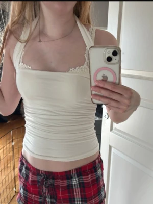 Vit halterneck topp - Snygg vit halterneck topp. Toppen är figurnära och har en ärmlös design med breda axelband som knyts i nacken. Perfekt för sommardagar eller att styla lager på lager.