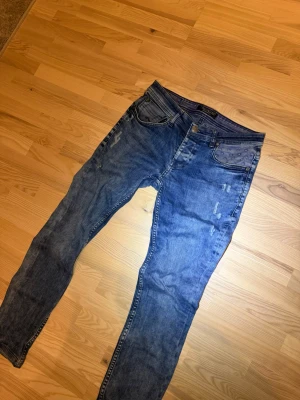 Blå skinny jeans med slitningar - Snygga blå skinny jeans med lätt slitna detaljer och klassisk femficksdesign. Jeansen har en smal passform och normal midja, perfekta för en trendig och avslappnad look. Tillverkade i mjukt denimtyg för skön komfort.