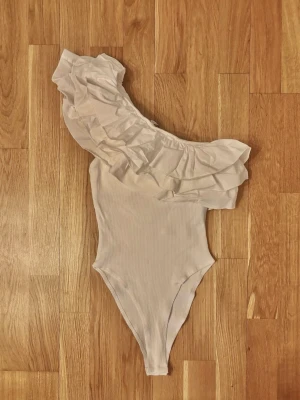Superfin vit body med volang - Zara🤍 - Superfin somrig vit body från Zara i storlek S 🤍One-shoulder-modell med söta volangdetaljer. Mjukt, ribbat och stretchigt material som sitter fint på kroppen.  Helt i nyskick- säljs då den tyvärr är för liten för mig.🥲🌸