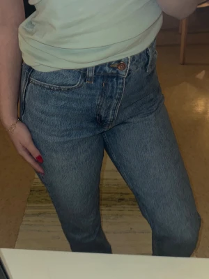 Blå högmidjade jeans från Zara - Säljer ett par klassiska blå jeans från Zara med hög midja och raka ben. Jeansen har fem fickor, bälteshällor och stängs med knapp och dragkedja. Perfekta till vardags och enkla att styla med olika toppar.