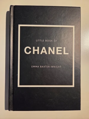 Little Book of Chanel bok - Stilren svart hårdinbunden bok med titeln 'Little Book of Chanel' av Emma Baxter-Wright. Boken har vit text och ram på omslaget och handlar om Coco Chanels liv, mode och inflytande. Perfekt för dig som gillar mode och ikoniska berättelser.