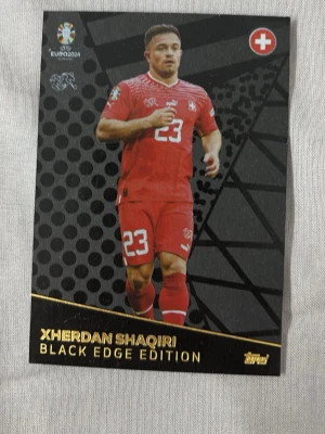 Xherdan Shaqiri Black Edge fotbollskort - Samlarfotbollskort från Topps Black Edge Edition med Xherdan Shaqiri i Schweiz landslagsdräkt. Kortet har svart bakgrund med guldtext och visar statistik och info om spelaren. Perfekt för dig som gillar fotboll och samlarkort. Köparen står för frakten.