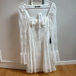 Vit spetsklänning från Gina Tricot - Supersöt vit kortklänning från Gina Tricot med långa ärmar, volangdetaljer vid ärmslut och knyt framtill. Klänningen är helt ny med prislapp, perfekt till student,konfirmation eller annan examen!😍 