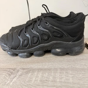 Svarta Nike sneakers  - Svarta sneakers från Nike med en chunky, bubblig sula och detaljerad ovandel i syntet och textil. Skorna har snörning och en sportig vibe, perfekt för dig som gillar streetwear. Diskret Nike-logga på insidan och VM Air-detalj bak.