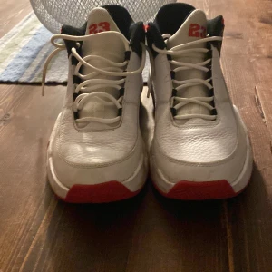 Nike Air Jordan 1 Mid Vit/Röd/Svart - Säljer ett par Nike Air Jordan 1 Mid i vitt skinn med röda och svarta detaljer. Skorna har klassisk snörning, röd 23-detalj på plösen och svart insida. Snygg och sportig siluett som sticker ut med sin färgkombination.