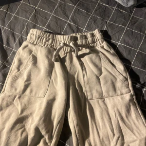 Beige mjukisbyxor från 157 i XS - Beiga mjukisbyxor från 157 med bred resår och snörning i midjan. Byxorna har stora fickor framtill och är gjorda i mjukt bomullsmaterial. Perfekta för chill dagar eller när du vill vara extra bekväm.